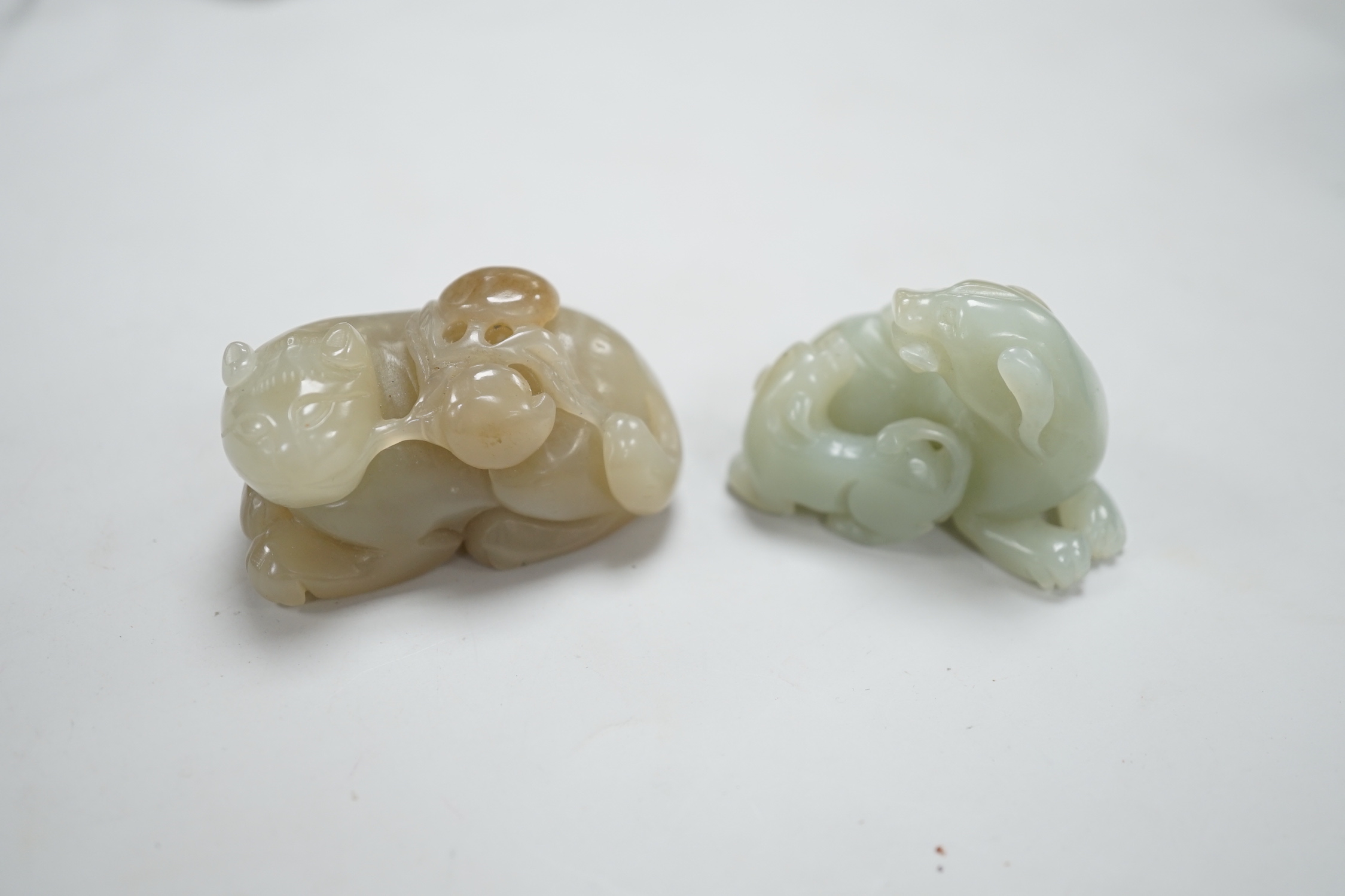 A Chinese celadon and brown jade figure of a cat biting a peach branch and a celadon jade group of a dog and puppy, cat biting a peach branch 5cm wide (2)